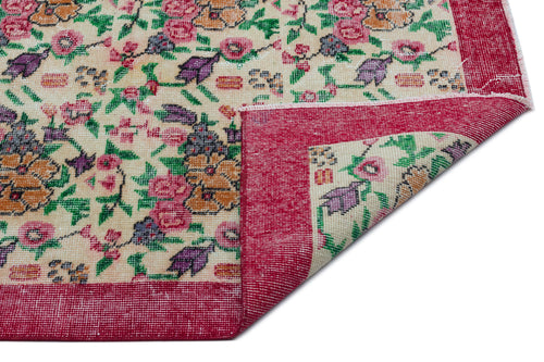 Load image 1 in gallery view. Cream rug with a floral pattern in pink, purple, and green, featuring a wide red border and a folded corner.
