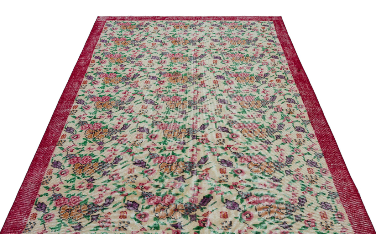 Cream rug with a red border and a repeating floral pattern in pink, orange, purple, and green.