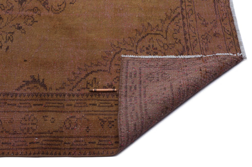 Load image 1 in gallery view. Brown distressed rug with a faded floral medallion pattern and a folded corner showing the reverse side.