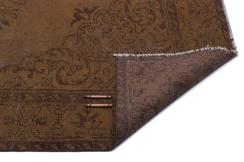 Load image 1 in gallery view. Brown vintage-style rug with a faded floral medallion pattern, shown with a corner folded over on a white background.