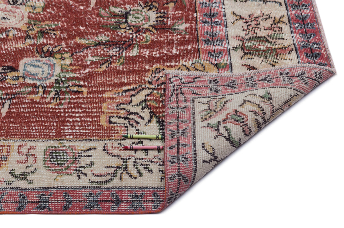 Distressed terracotta and cream rug with a floral medallion pattern and a folded corner, isolated on a white background.