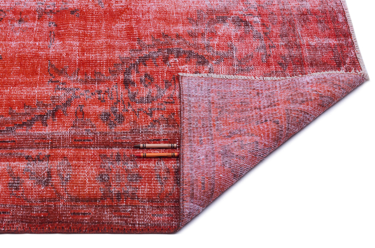 Distressed red and dark brown vintage-style rug with a faded floral medallion pattern, shown with a folded corner.
