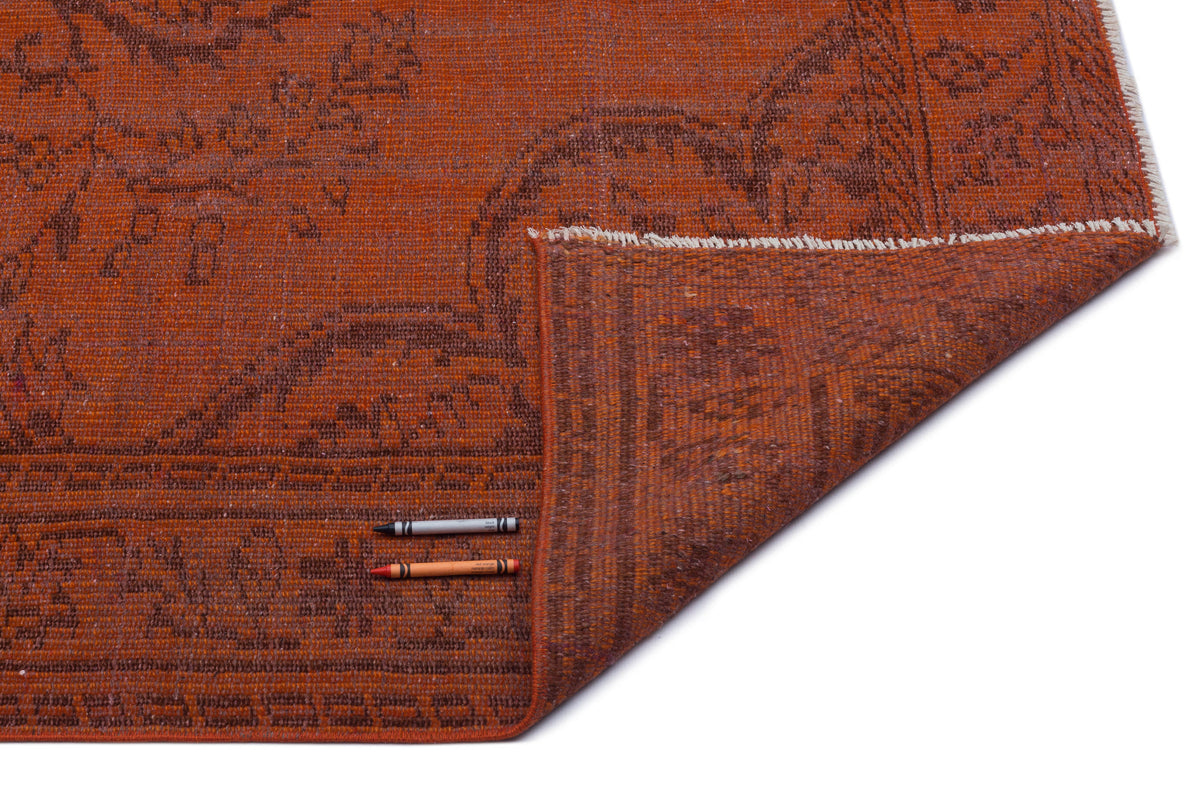 Burnt orange rug with a dark brown traditional medallion pattern, shown with a corner folded back on a white background.