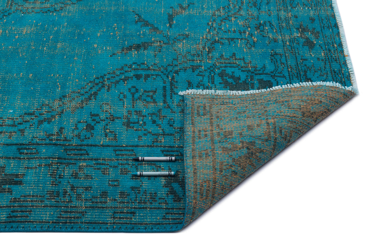 Turquoise and charcoal distressed traditional rug with a folded corner, isolated on a white background.