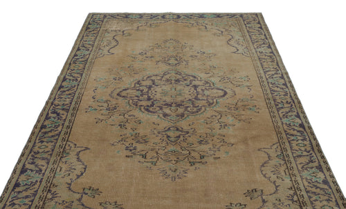 Load image 1 in gallery view. Tan vintage-style rug with a dark purple and teal central medallion and ornate border on a white background.