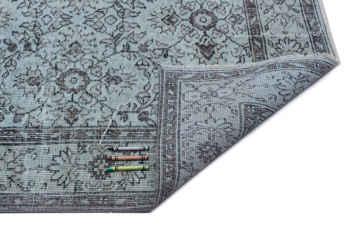 Light blue and brown distressed traditional medallion rug with a folded corner, isolated on a white background.