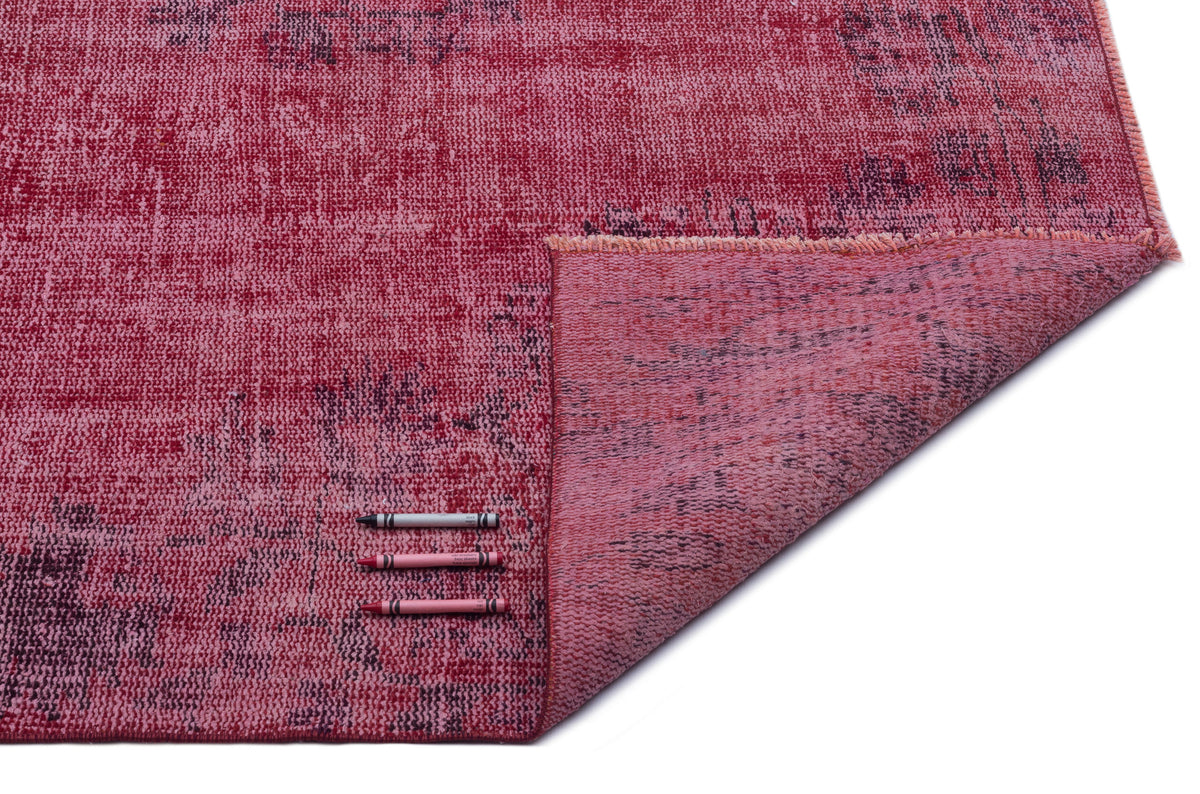 Distressed magenta and dark purple vintage-style rug with a folded corner, shown with three color reference crayons.