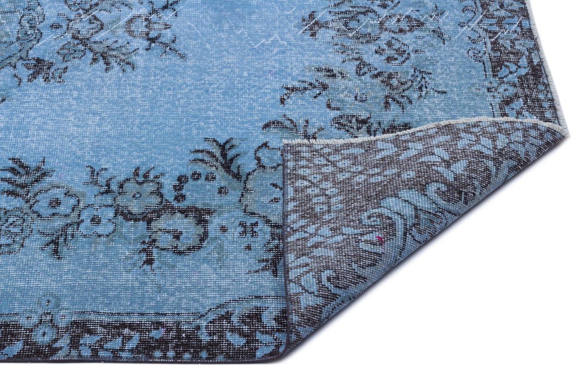 Light blue rug with a dark grey floral pattern and a folded corner revealing the woven backing.