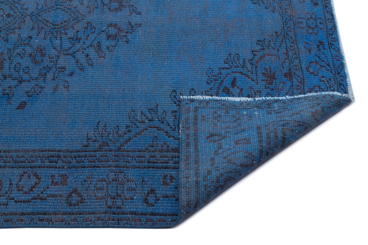 Deep blue rug with a black traditional floral pattern and a folded corner revealing the underside texture.