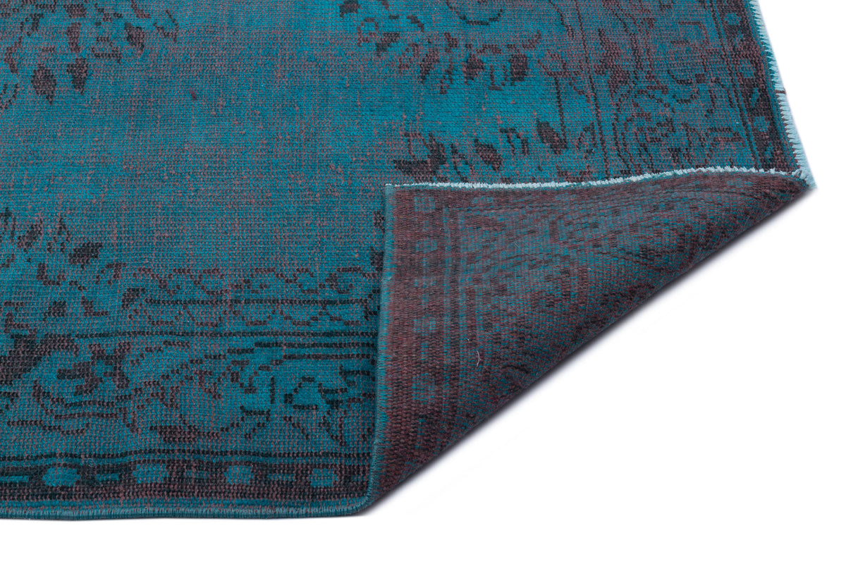 Teal and charcoal distressed rug with a traditional floral pattern, shown with a corner folded over.