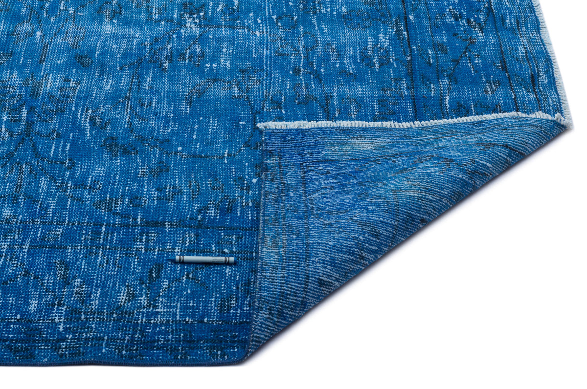 Distressed blue rug with a faded black traditional pattern and a folded corner, isolated on a white background.