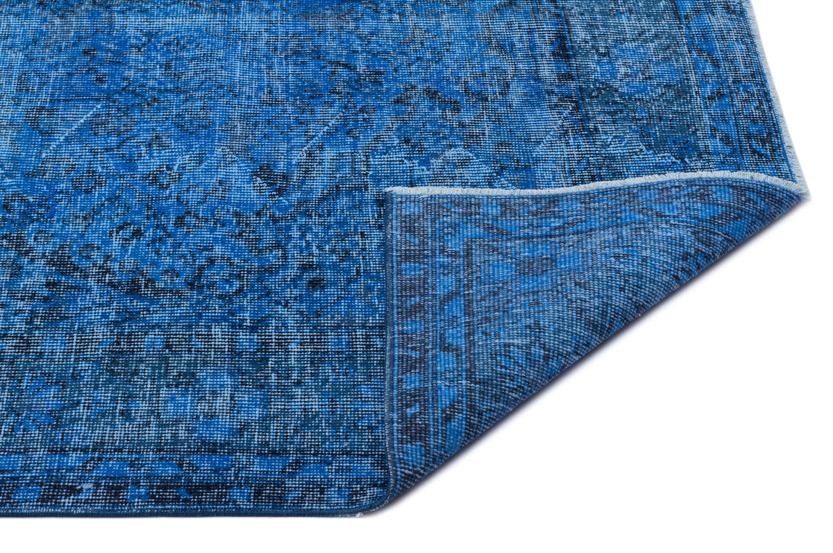 Blue distressed traditional rug with a faded floral medallion pattern, shown with a folded corner on a white background.