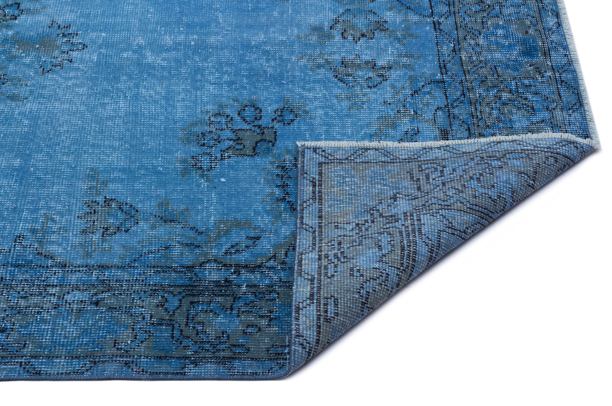 Bright blue distressed rug with a dark grey floral medallion pattern and a folded corner on a white background.