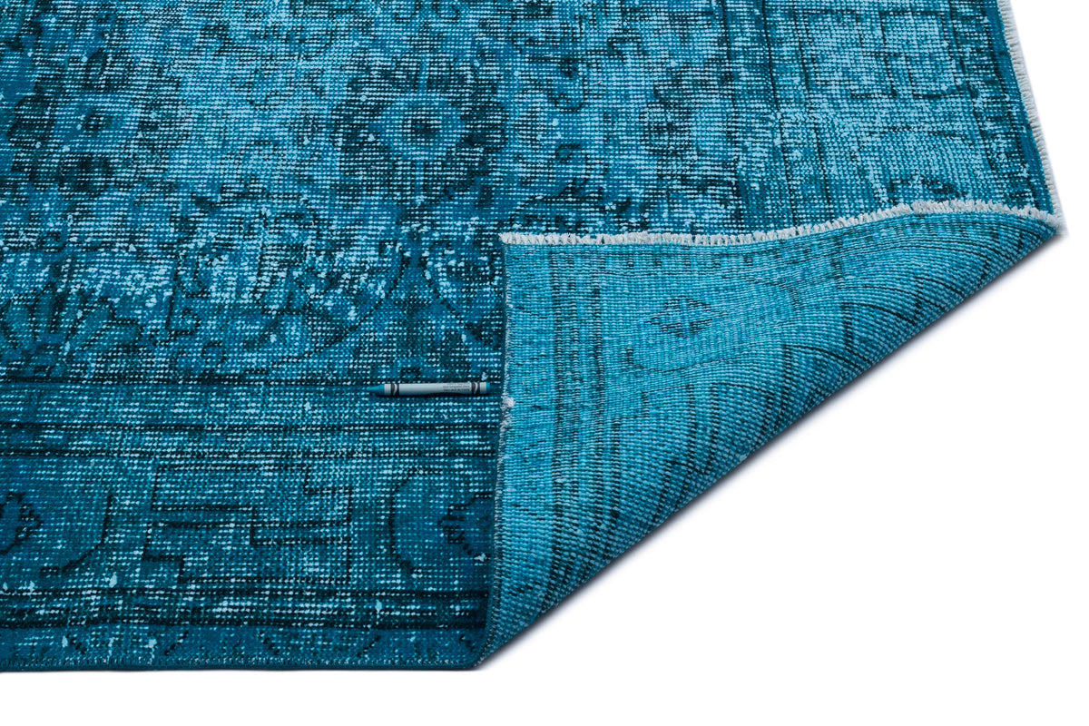 Bright blue distressed rug with a traditional medallion pattern, shown with a corner folded over on a white background.