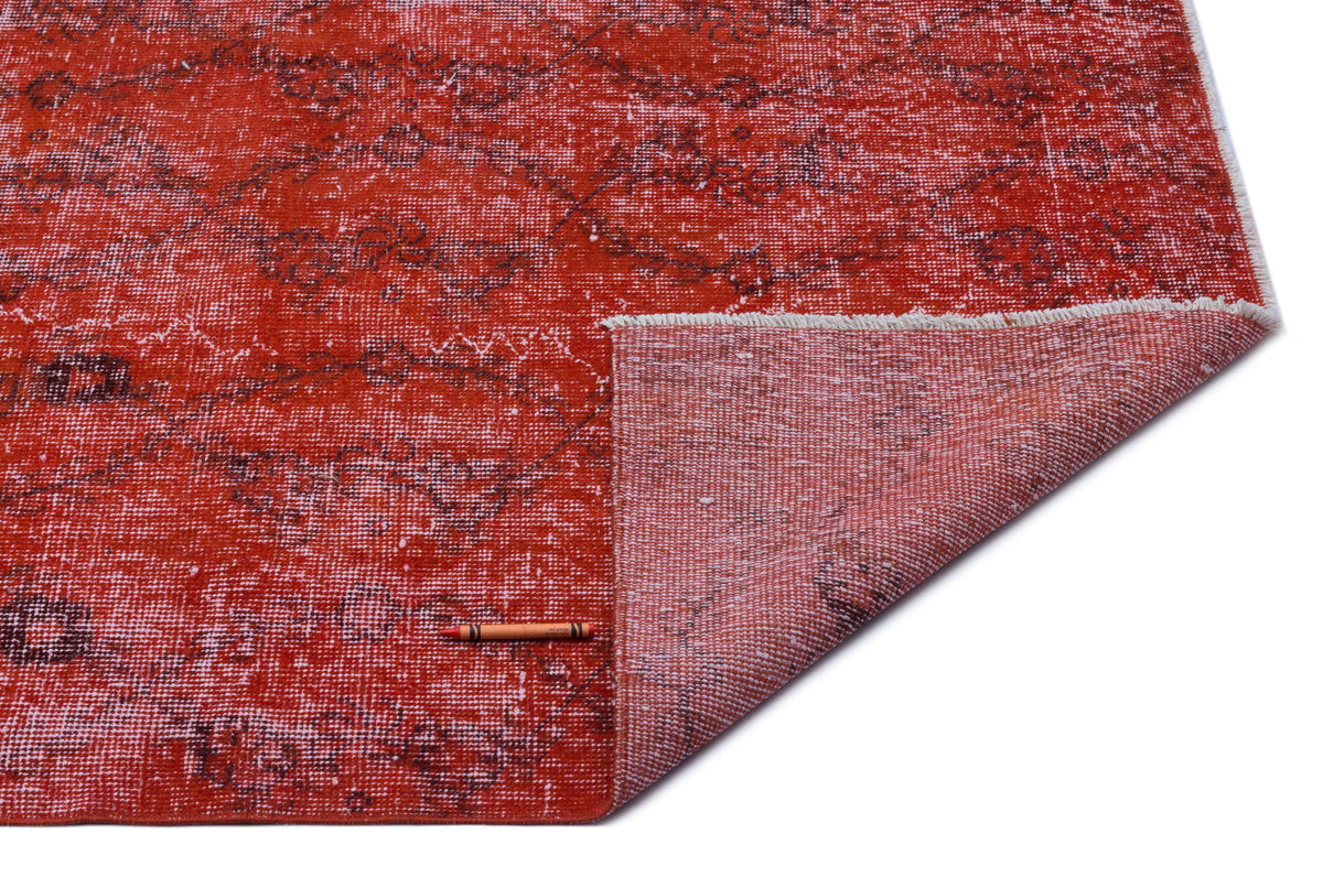 Distressed red rug with a dark floral pattern and a folded corner showing the woven backing on a white background.