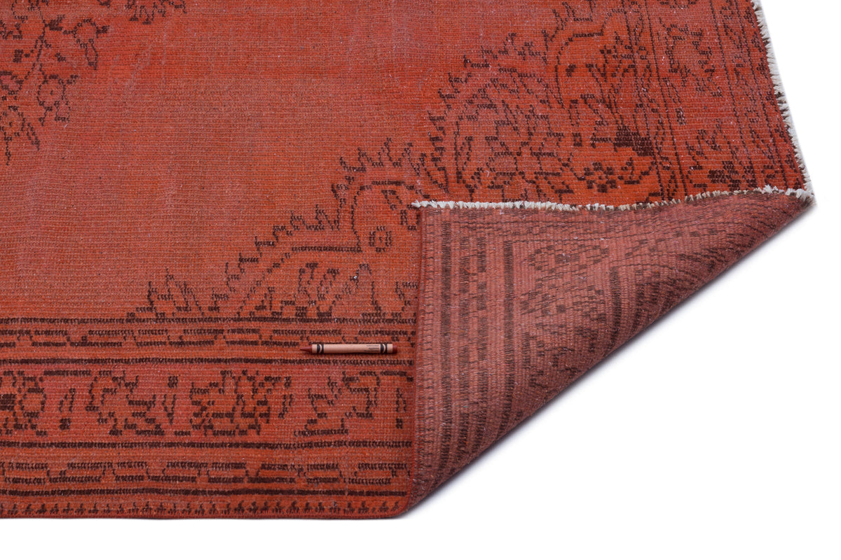 Terracotta rug with a dark brown floral border and a folded corner revealing the woven backing, on a white background.