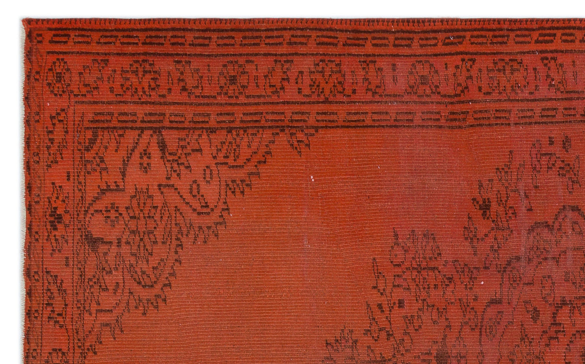 Rust-red rug with a black linear border and intricate floral corner medallion pattern.