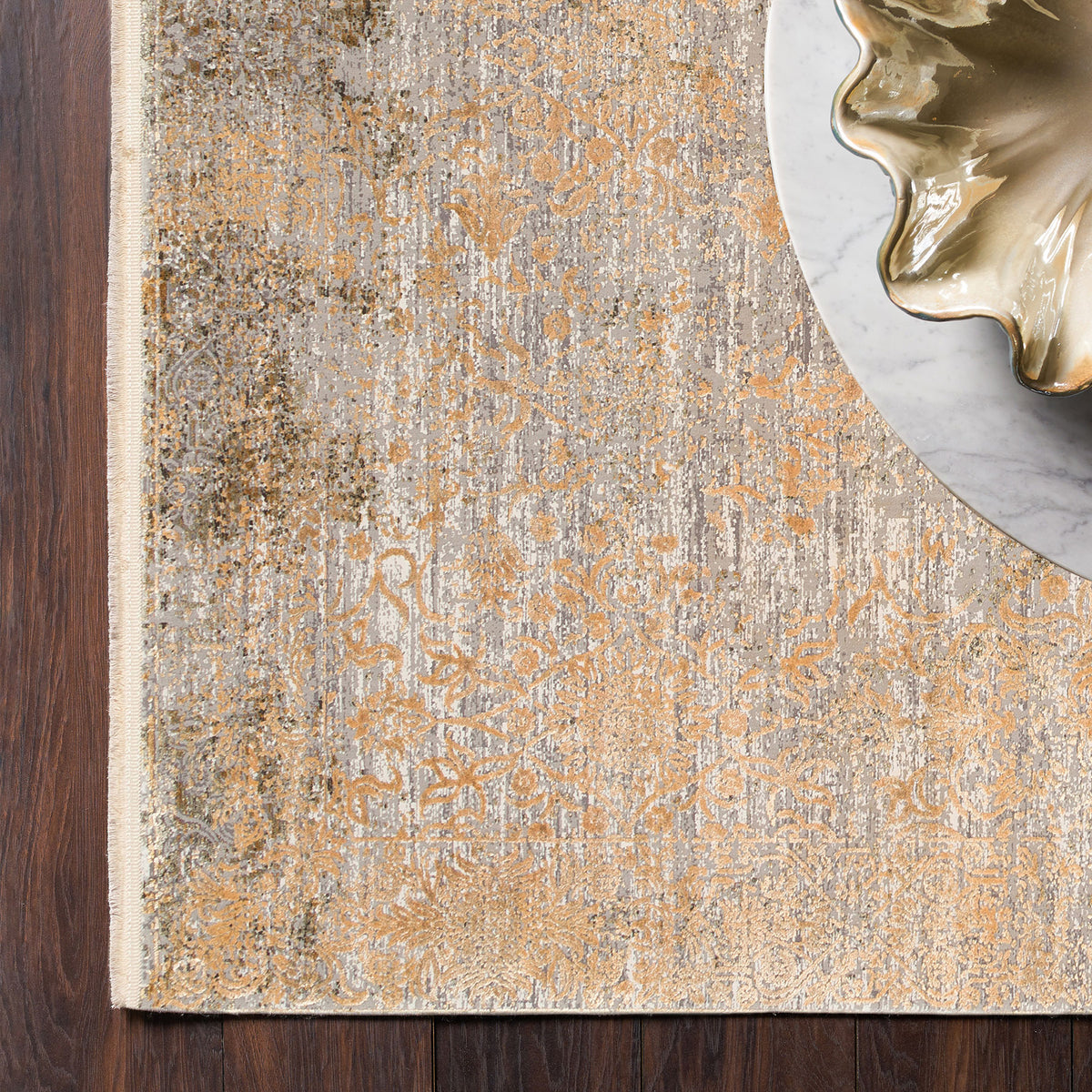 Grey and gold distressed floral medallion rug on a dark wood floor with a marble table edge.