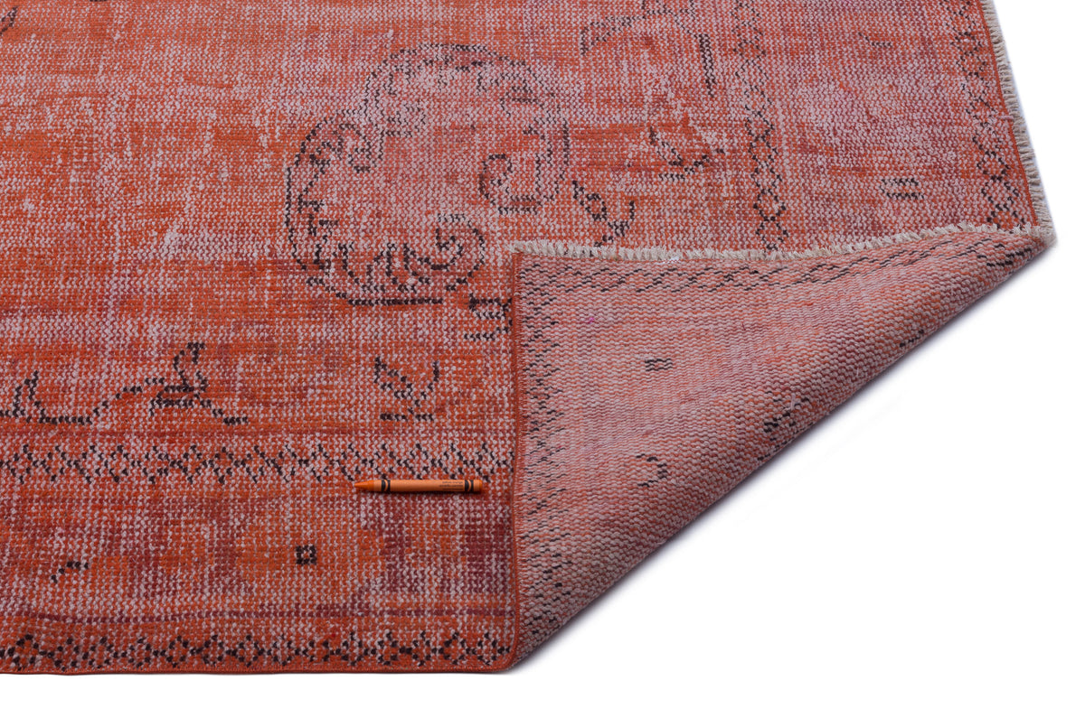 Distressed orange rug with a faded black medallion pattern and a folded corner showing the underside, white background.