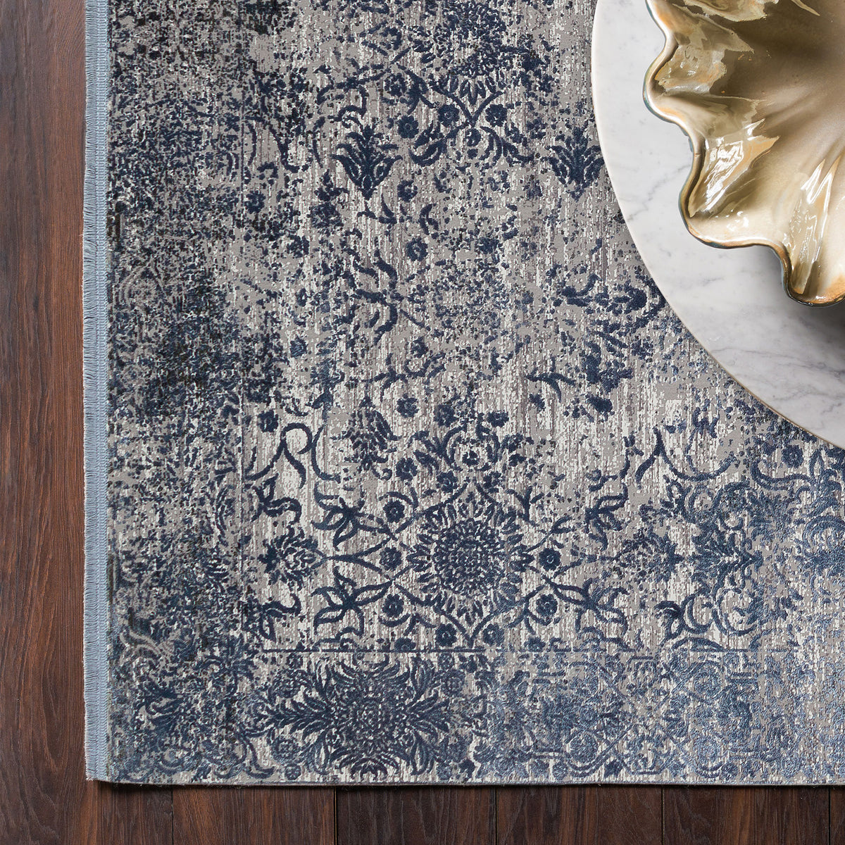 Navy and grey distressed floral medallion rug on a dark wood floor with a marble side table.