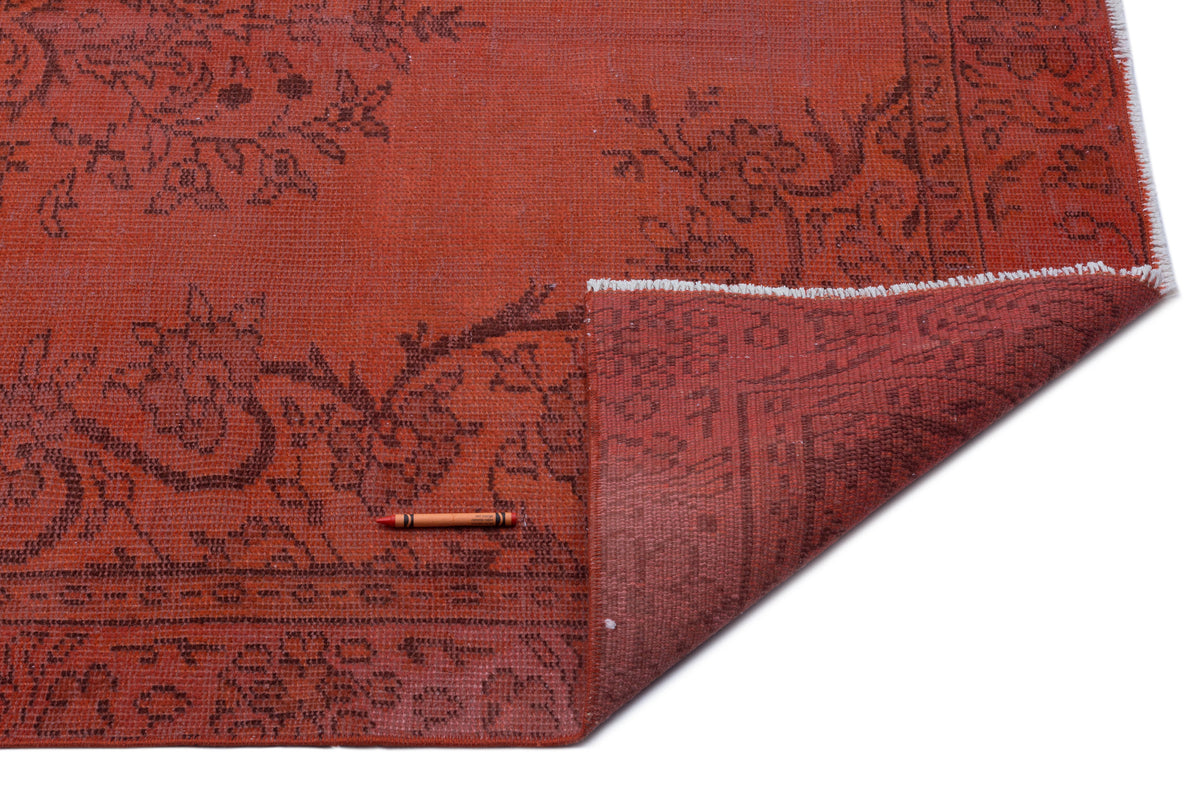Distressed terracotta rug with a dark brown floral pattern and a folded corner showing the reverse side.