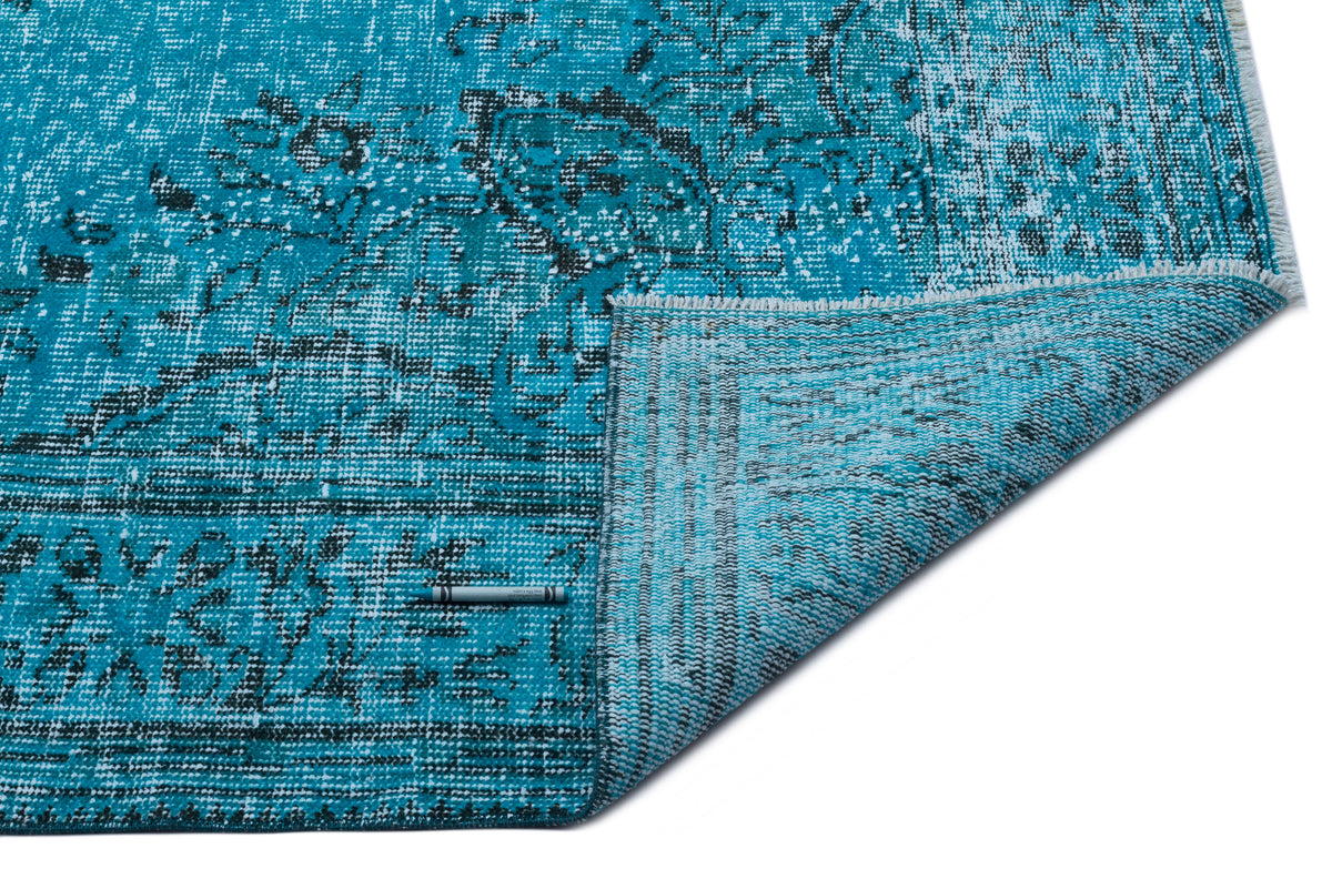 Turquoise and black distressed traditional rug with a folded corner showing the underside, isolated on white.