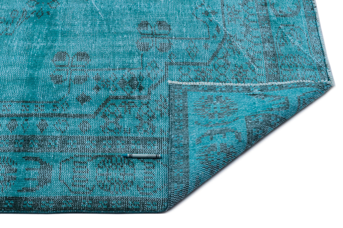 Turquoise and black distressed rug with a traditional medallion pattern, shown with a corner folded over on white.