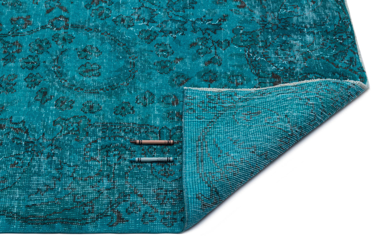 Teal rug with a distressed black floral medallion pattern, shown with a corner folded back on a white background.