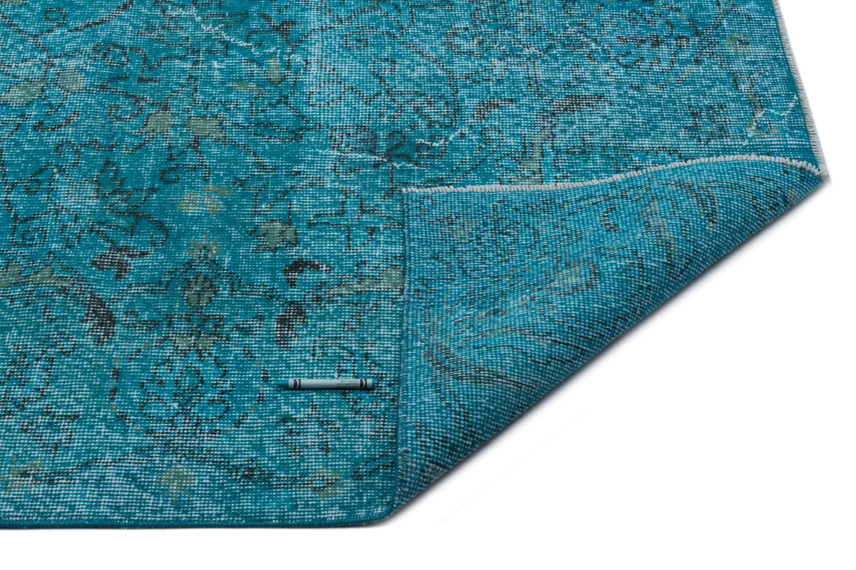 Teal distressed rug with a faded floral pattern and a folded corner, isolated on a white background.