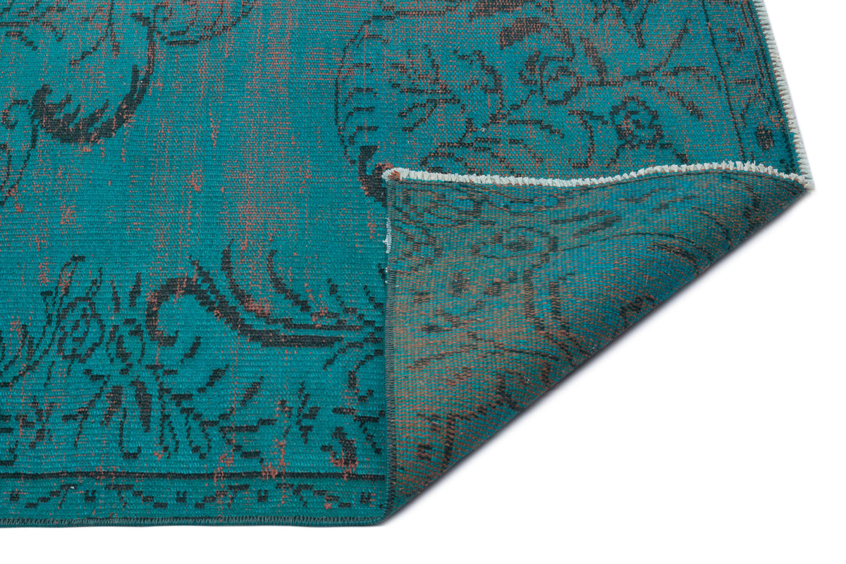 Teal rug with a distressed black floral pattern and a folded corner revealing the underside.