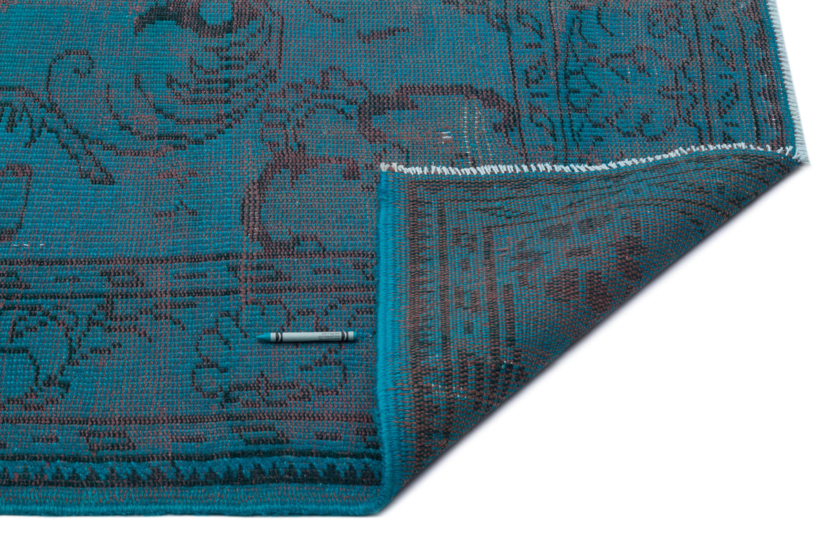 Teal and charcoal distressed rug with a traditional floral pattern, shown with a corner folded over on a white background.