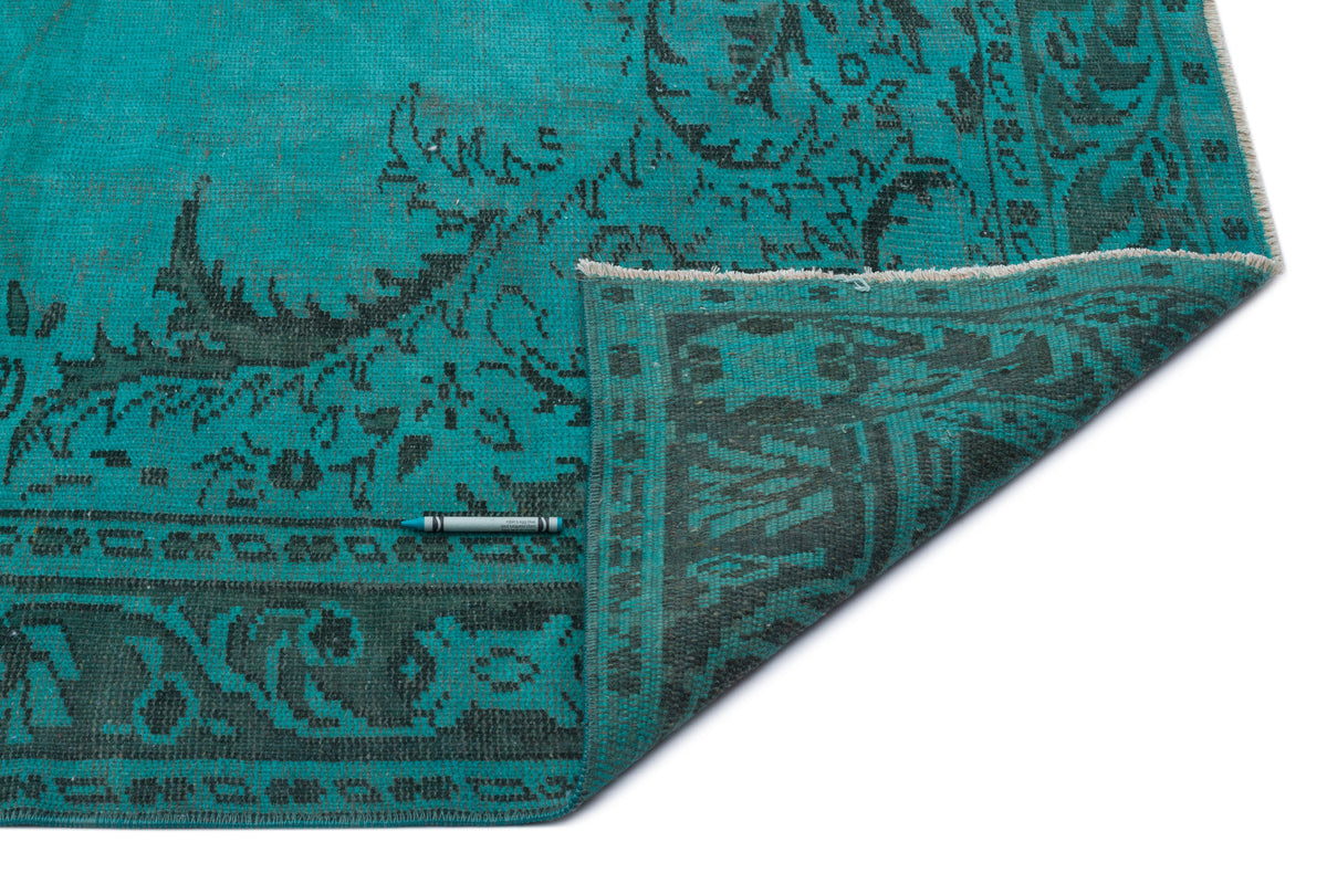 Turquoise and charcoal distressed rug with a traditional floral pattern, shown with a corner folded over.