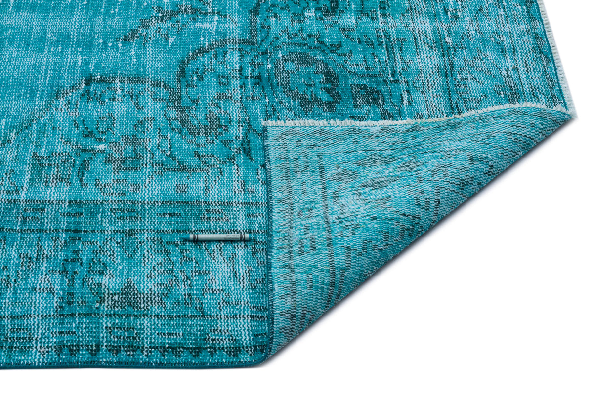 Turquoise and dark grey distressed medallion rug with a folded corner showing the underside and fringe.