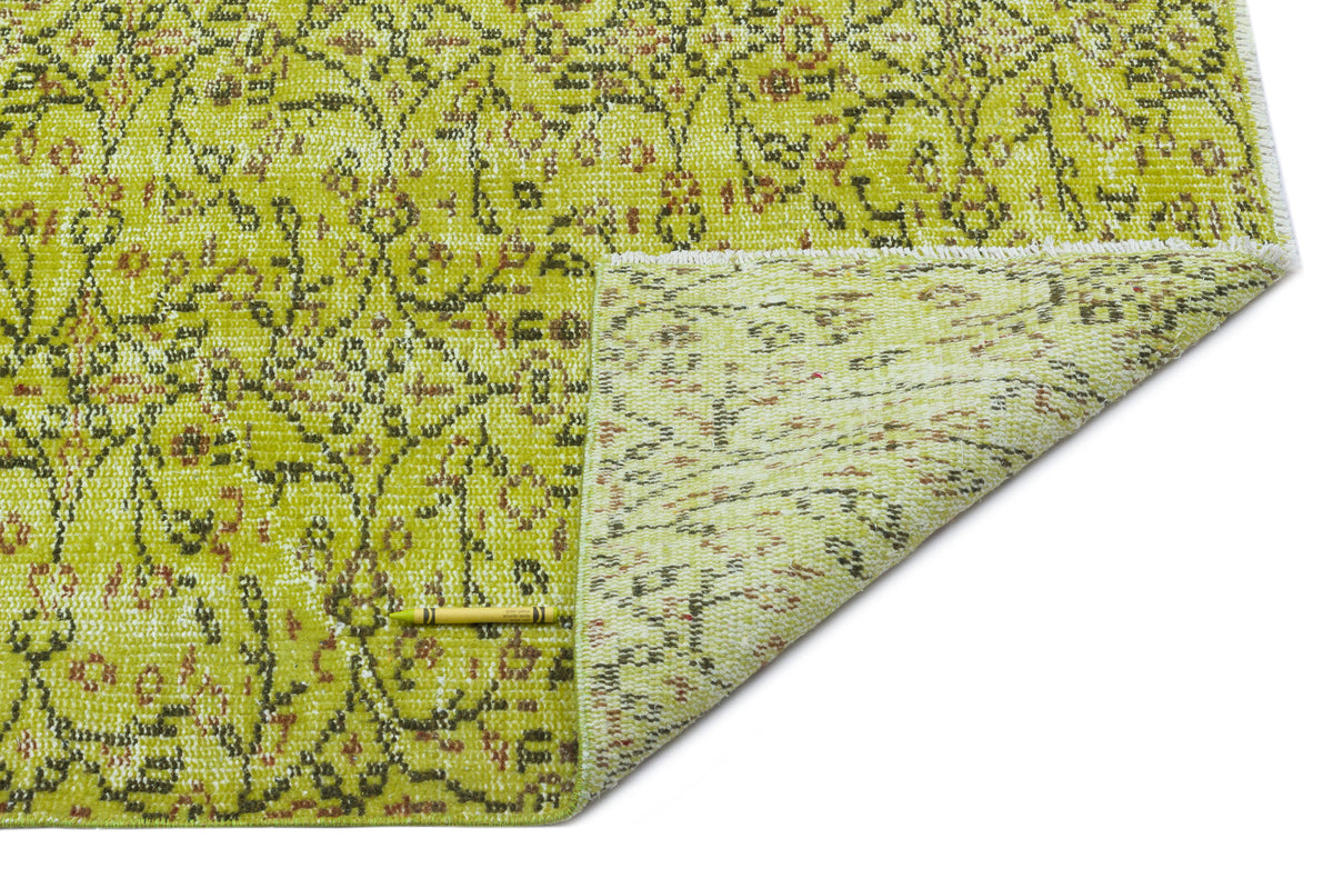 Chartreuse and olive green rug with a distressed floral pattern, shown with a corner folded over on a white background.