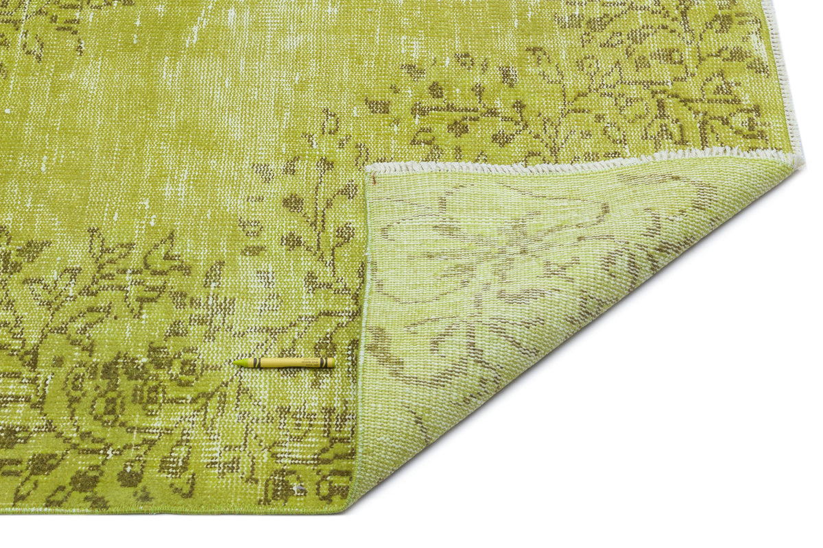 Chartreuse and olive green distressed floral rug with a folded corner showing the woven backing on a white background.