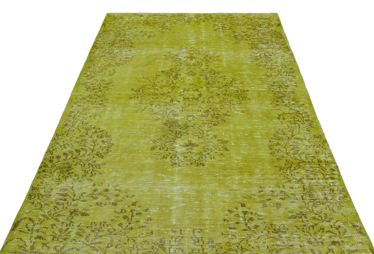 Chartreuse distressed rug with a faded central floral medallion and border pattern on a white background.