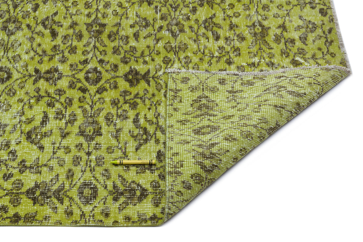 Chartreuse and dark brown floral patterned rug with a folded corner, isolated on a white background.