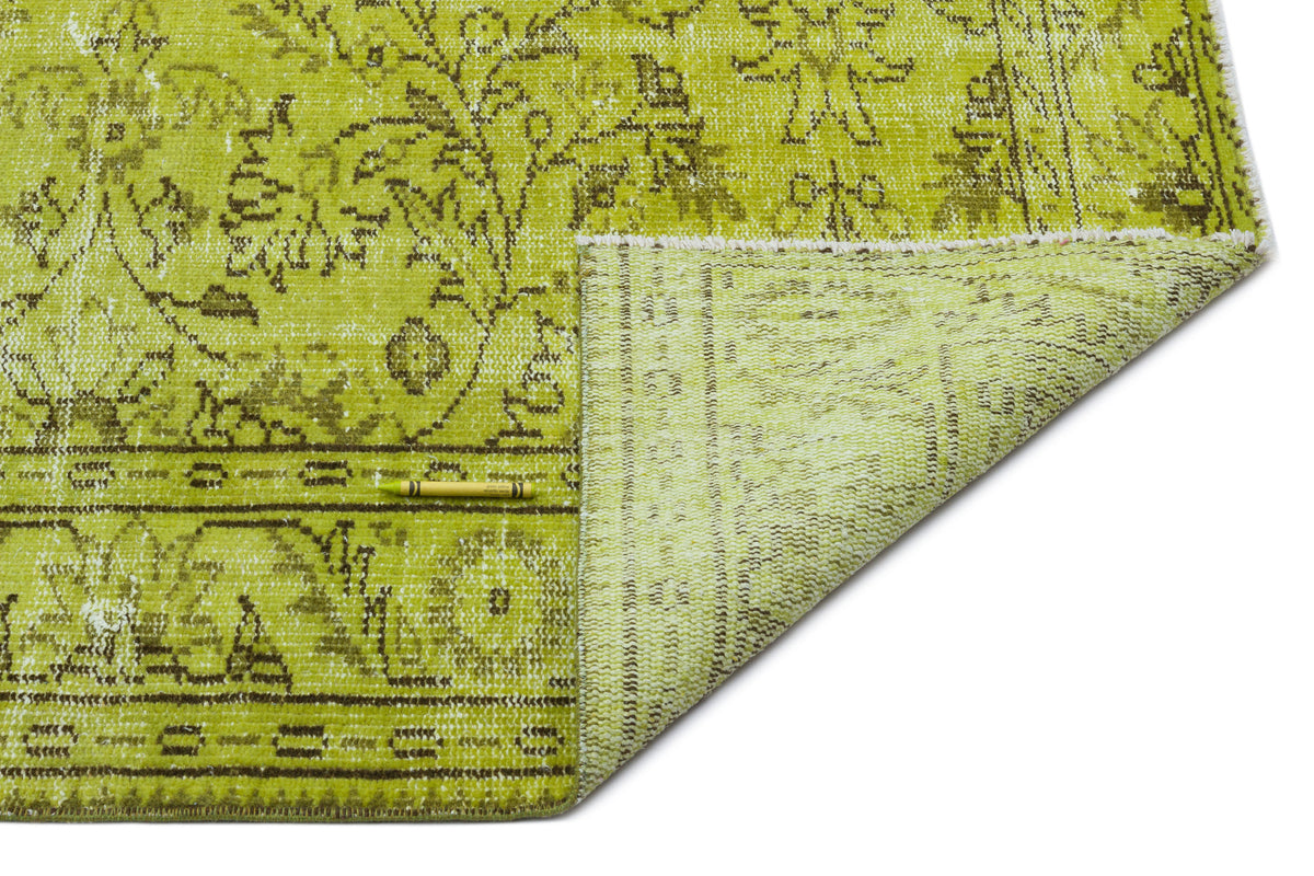 Chartreuse and brown distressed rug with a traditional floral medallion pattern, shown with a corner folded over.