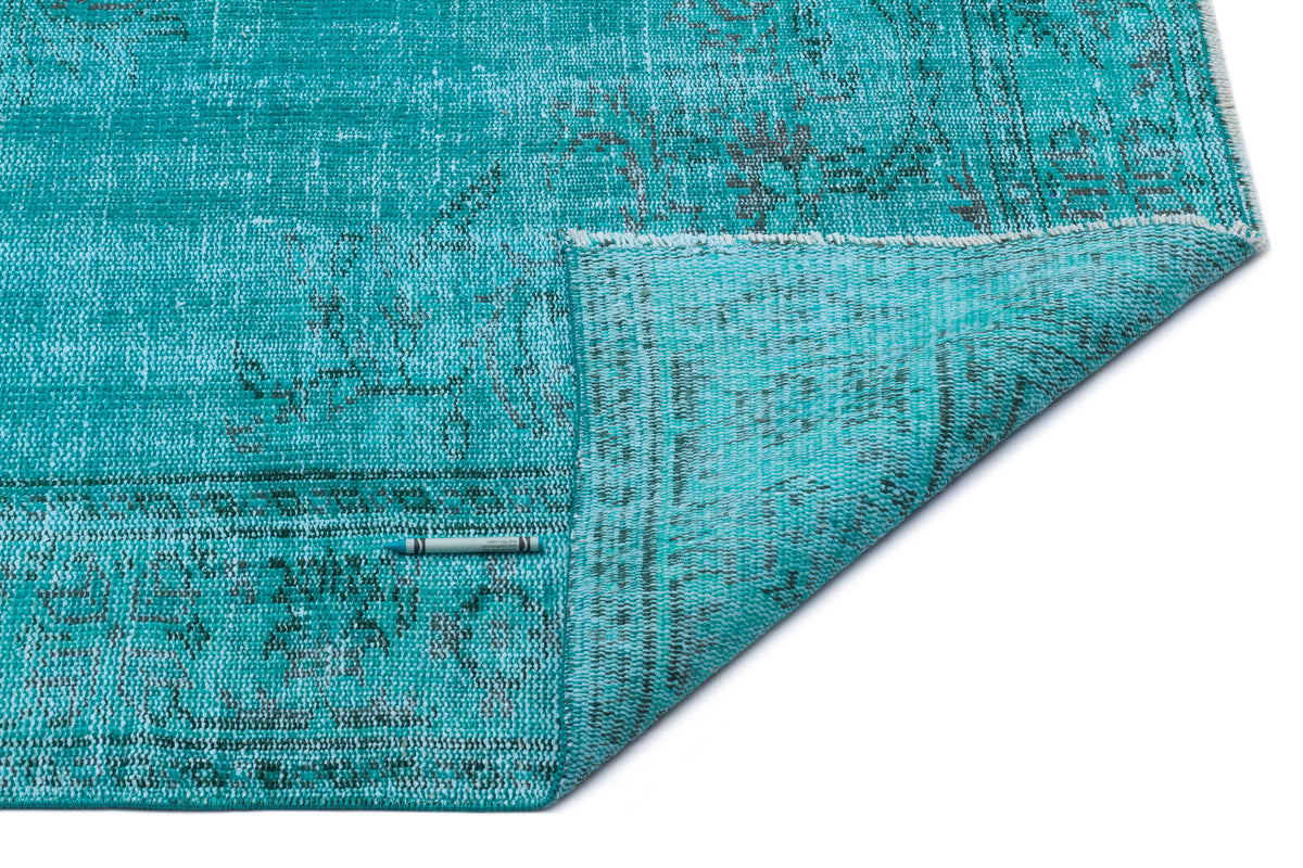 Distressed turquoise rug with a faded traditional pattern and a folded corner, isolated on a white background.