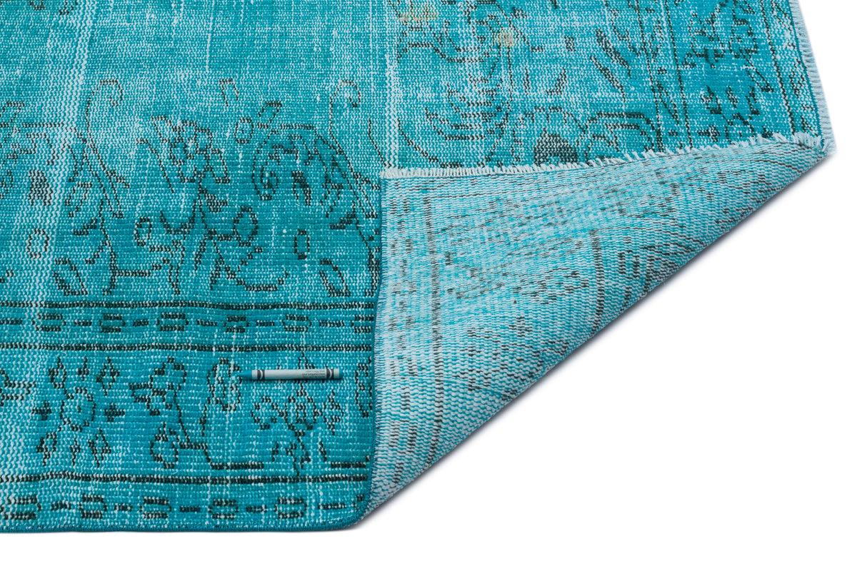 Turquoise distressed rug with a faded black floral pattern and a folded corner, isolated on a white background.