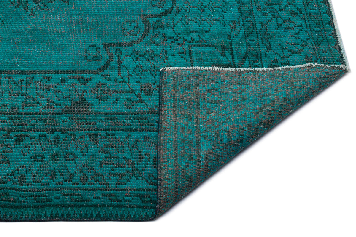 Teal and charcoal distressed rug with a traditional medallion pattern, shown with a folded corner on a white background.