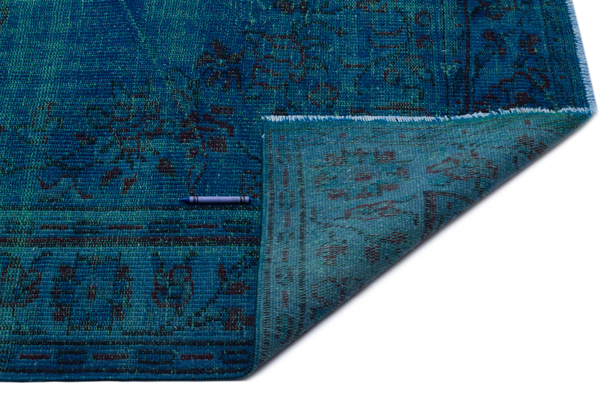 Teal and blue distressed rug with a traditional floral pattern, shown with a corner folded over on a white background.