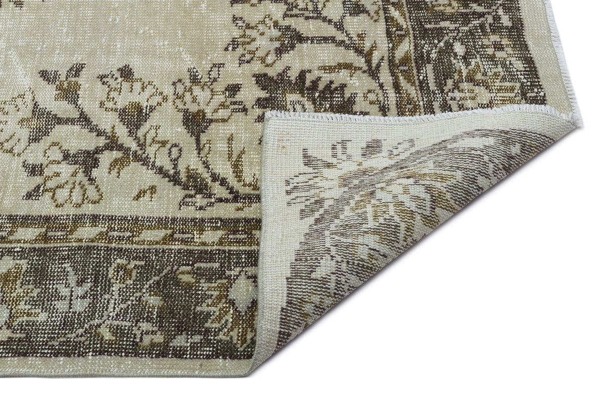 Beige and brown traditional floral rug with a distressed finish, shown with a corner folded over on a white background.