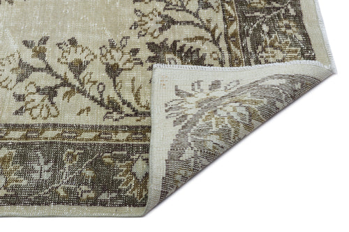 Load image 1 in gallery view. Beige and brown traditional floral rug with a distressed finish, shown with a corner folded over on a white background.