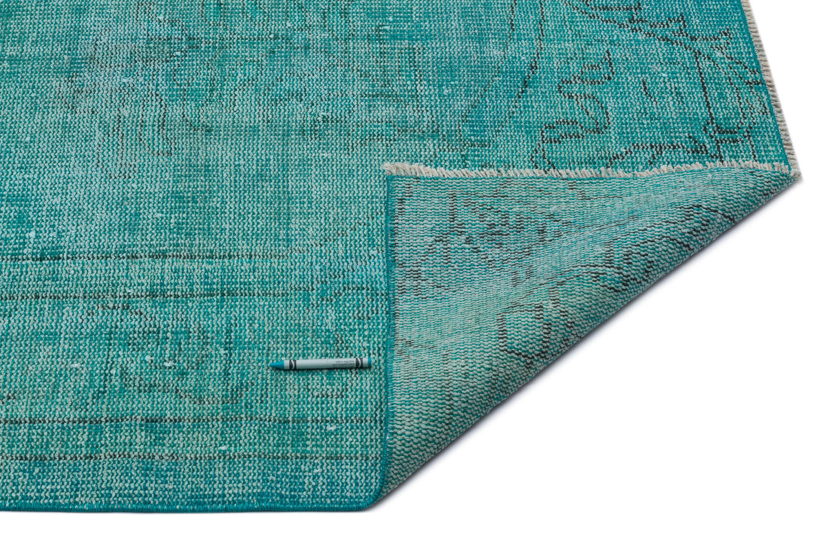 Teal distressed rug with a faded traditional pattern, shown with a corner folded over on a white background.