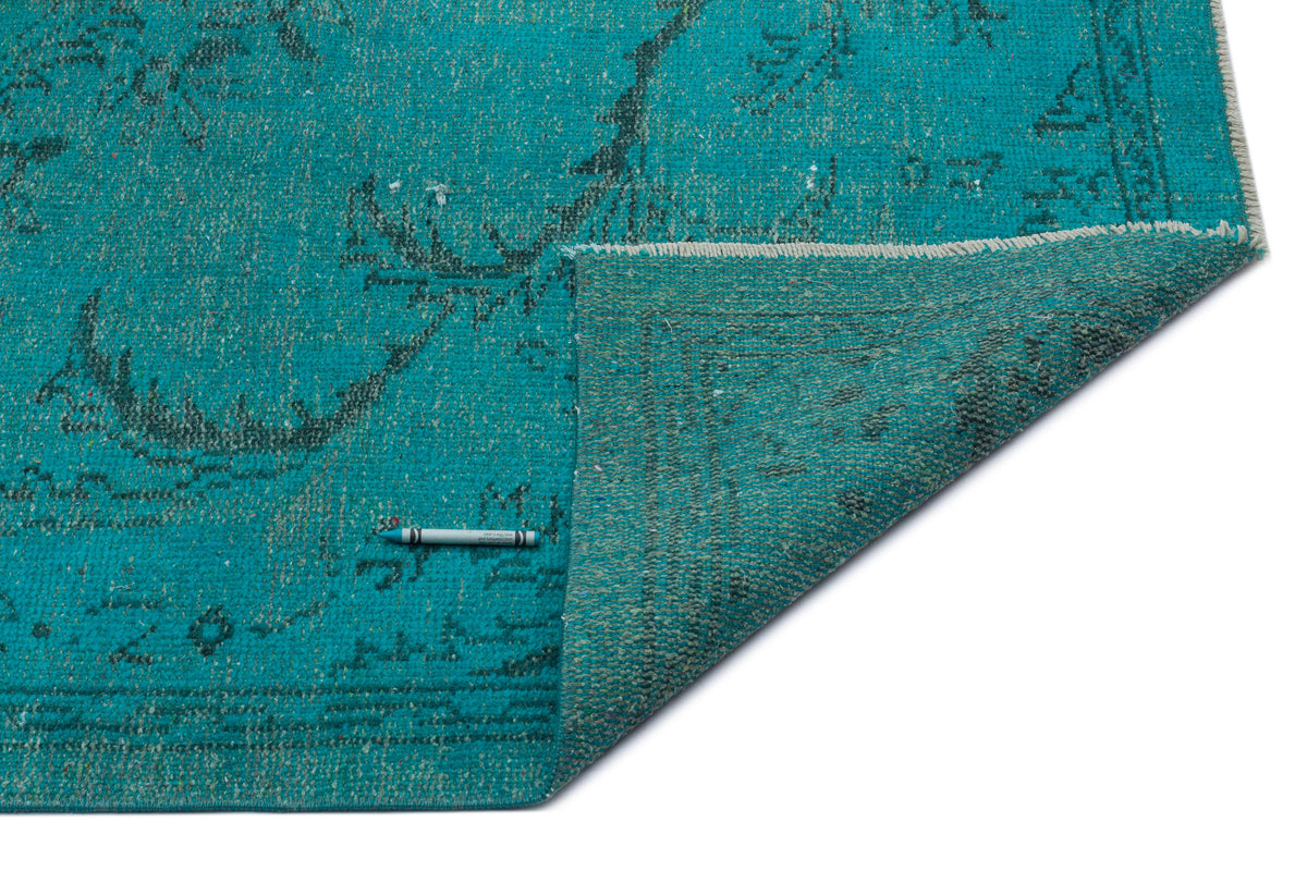 Teal distressed rug with a faded floral pattern, shown with a corner folded over on a white background.