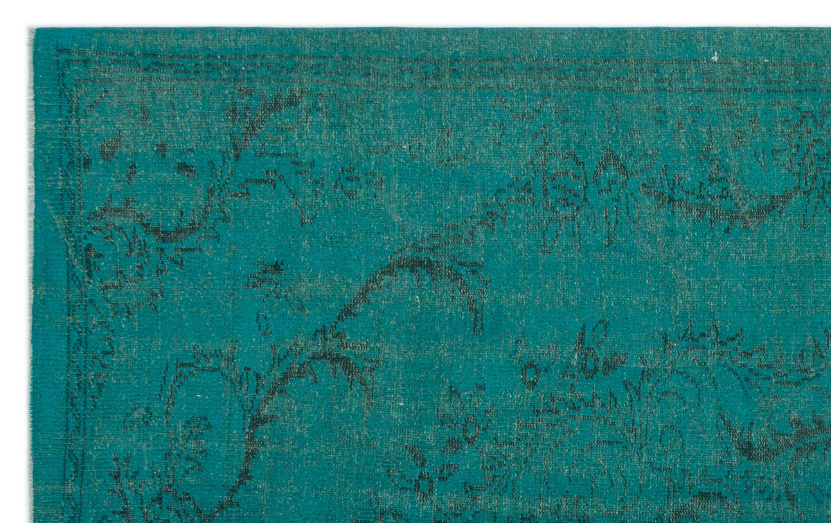 Teal rug with a dark, distressed floral pattern and a thin border.