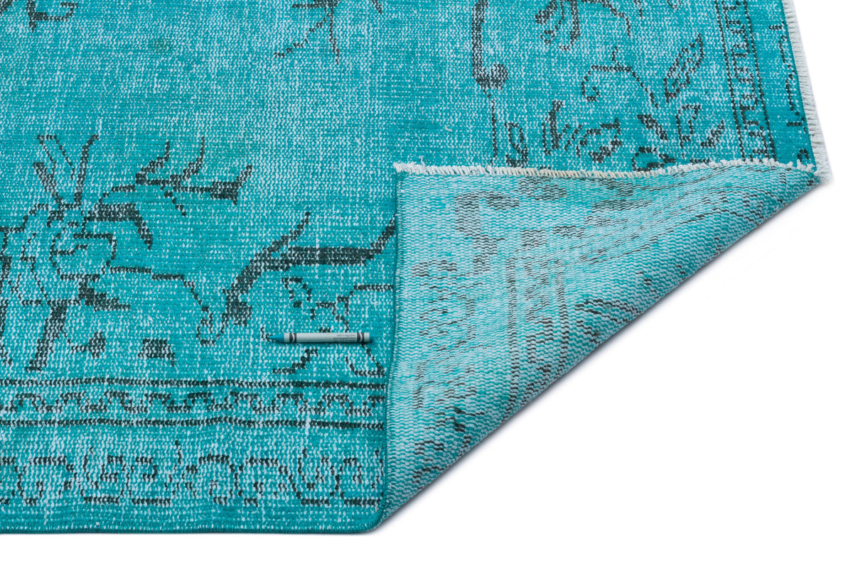 Turquoise distressed rug with a dark grey floral pattern and a folded corner showing the underside.