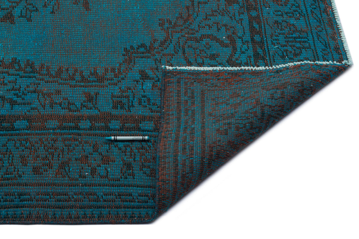 Teal and dark brown rug with a traditional floral medallion pattern, shown with a corner folded over on a white background.
