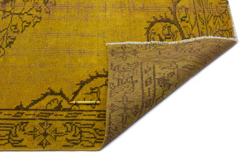 Load image 1 in gallery view. Mustard yellow and brown distressed rug with a traditional floral medallion pattern, shown with a corner folded over.